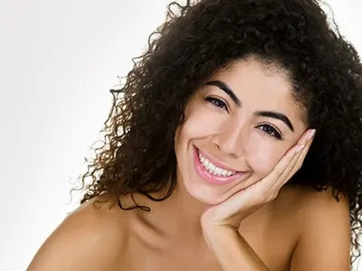 A smiling woman with long curly dark hair rests her chin on her hand