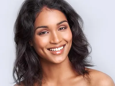 A smiling woman with wavy dark hair and bare shoulders against a soft lavender background