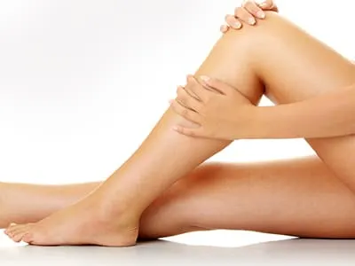 A woman sits on a white floor with her bare legs stretched out, one hand on her knee