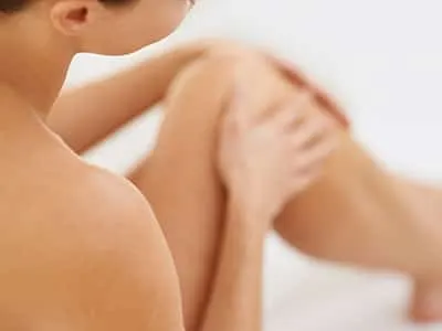 A woman sits with her bare legs drawn up and a hand on her knee, softly out of focus