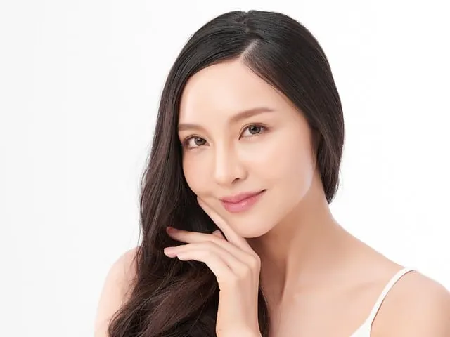 A woman with long dark hair rests her hand against her cheek against a white background.