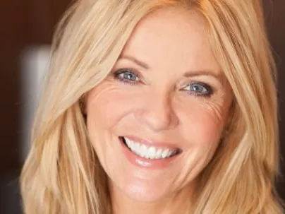 A smiling woman with long blonde hair and fine lines around her eyes