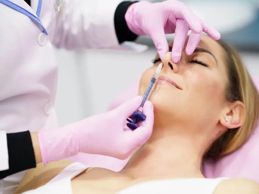 Woman smiling while receiving a liquid rhinoplasty to lift the tip of her nose.