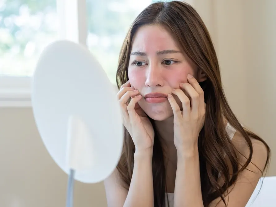 Woman looking in mirror at her red and inflamed face due to spring skin allergies