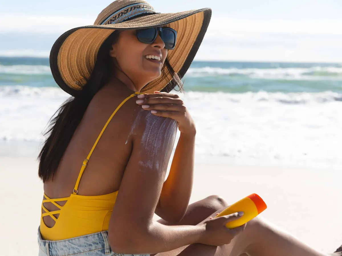 Mujer en la playa aplicándose protector solar en los hombros para protegerse contra el melanoma y el cáncer de piel.