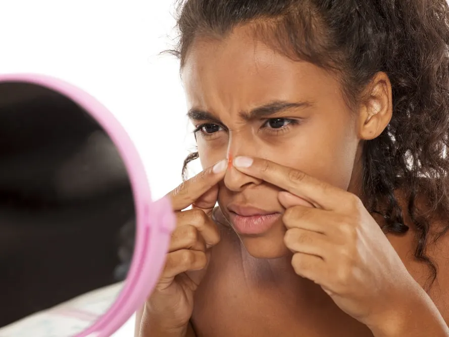 Woman touching pimple on nose while looking in mirror