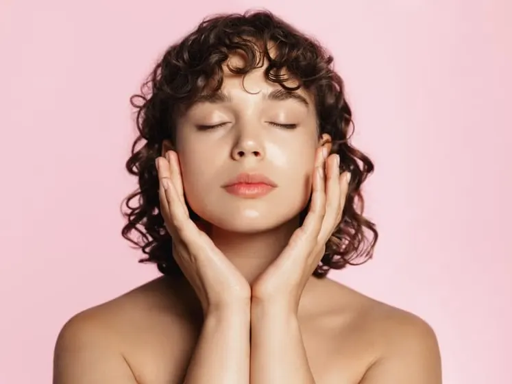 Young woman with glowing skin gently touching her face after a chemical peel treatment