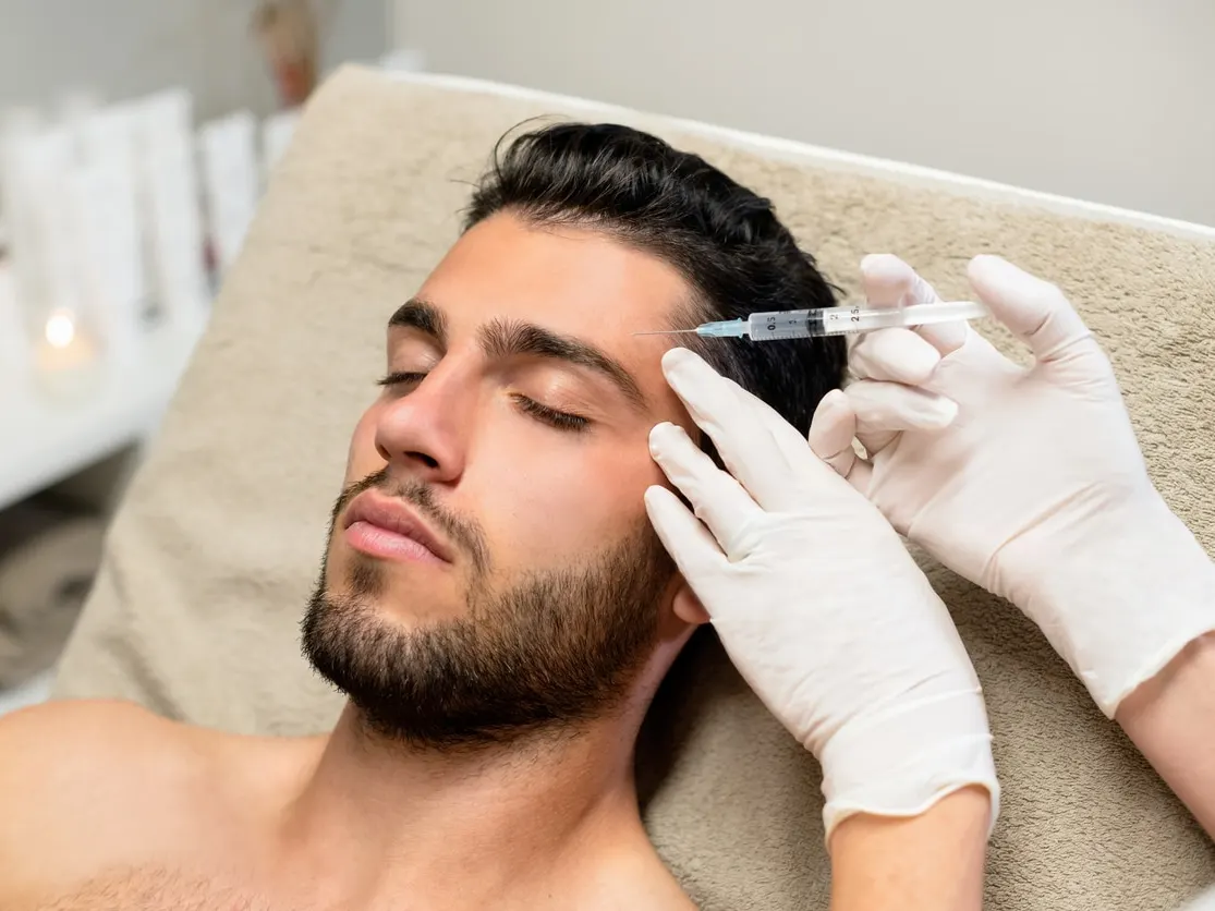 Man receiving a cosmetic injectable treatment near the temple in a clinical setting.