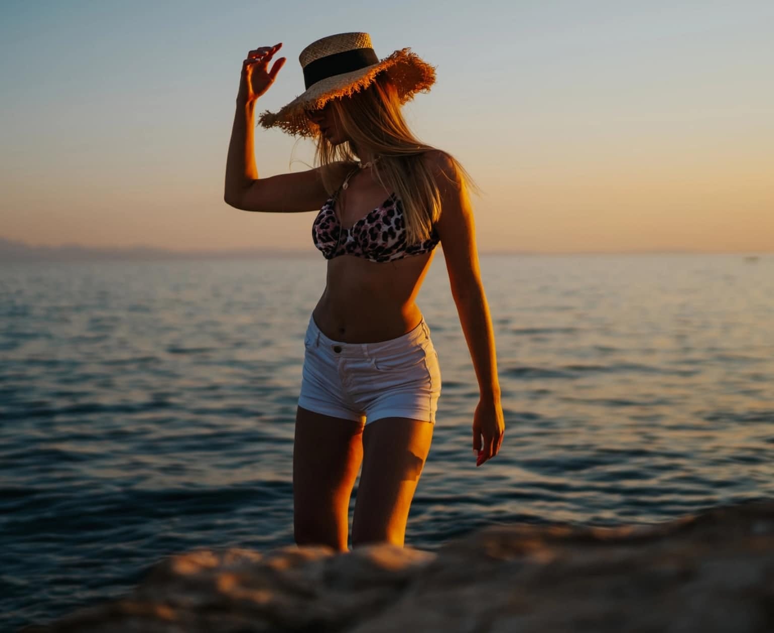 A model in a straw hat standing by the sea at sunset