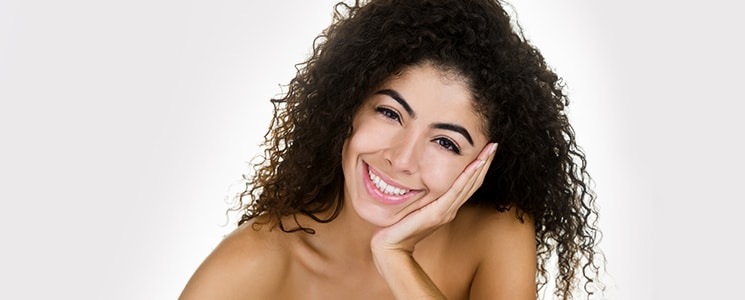 A smiling woman with long curly dark hair rests her chin on her hand