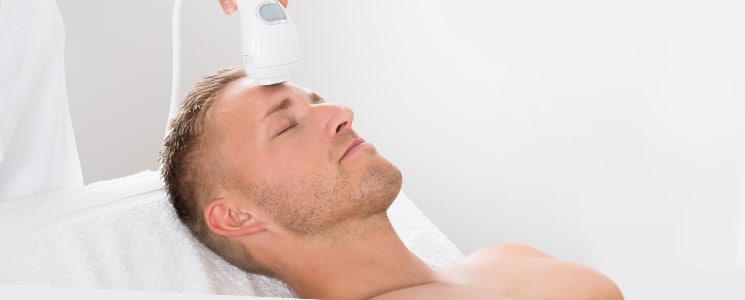 A man lies back with eyes closed as a white handheld device is held to his forehead