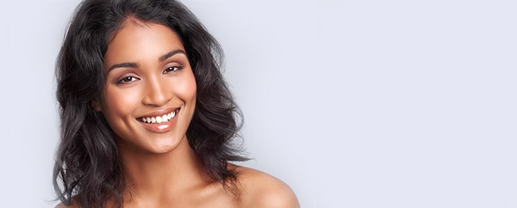 A smiling woman with wavy dark hair and bare shoulders against a soft lavender background