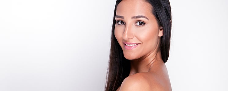 A woman with long straight dark hair looks back over her bare shoulder with a slight smile