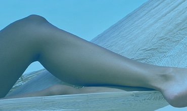 A model’s smooth bare legs resting on a hammock, tinted blue