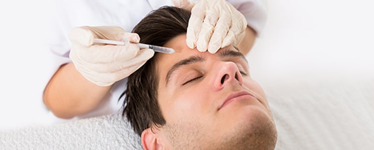 A clinician in gloves holds a syringe to a man's forehead as he lies with eyes closed