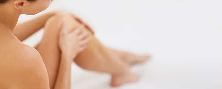 A woman sits with her bare legs drawn up and a hand on her knee, softly out of focus