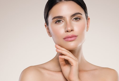 A model with slicked-back dark hair and natural makeup rests her hand under her chin.
