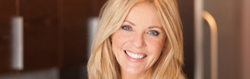 A smiling woman with long blonde hair and fine lines around her eyes