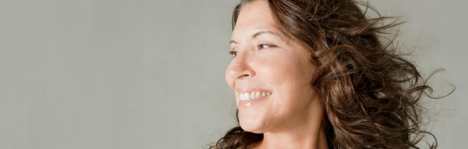 A smiling model with curly brown hair blowing in the wind