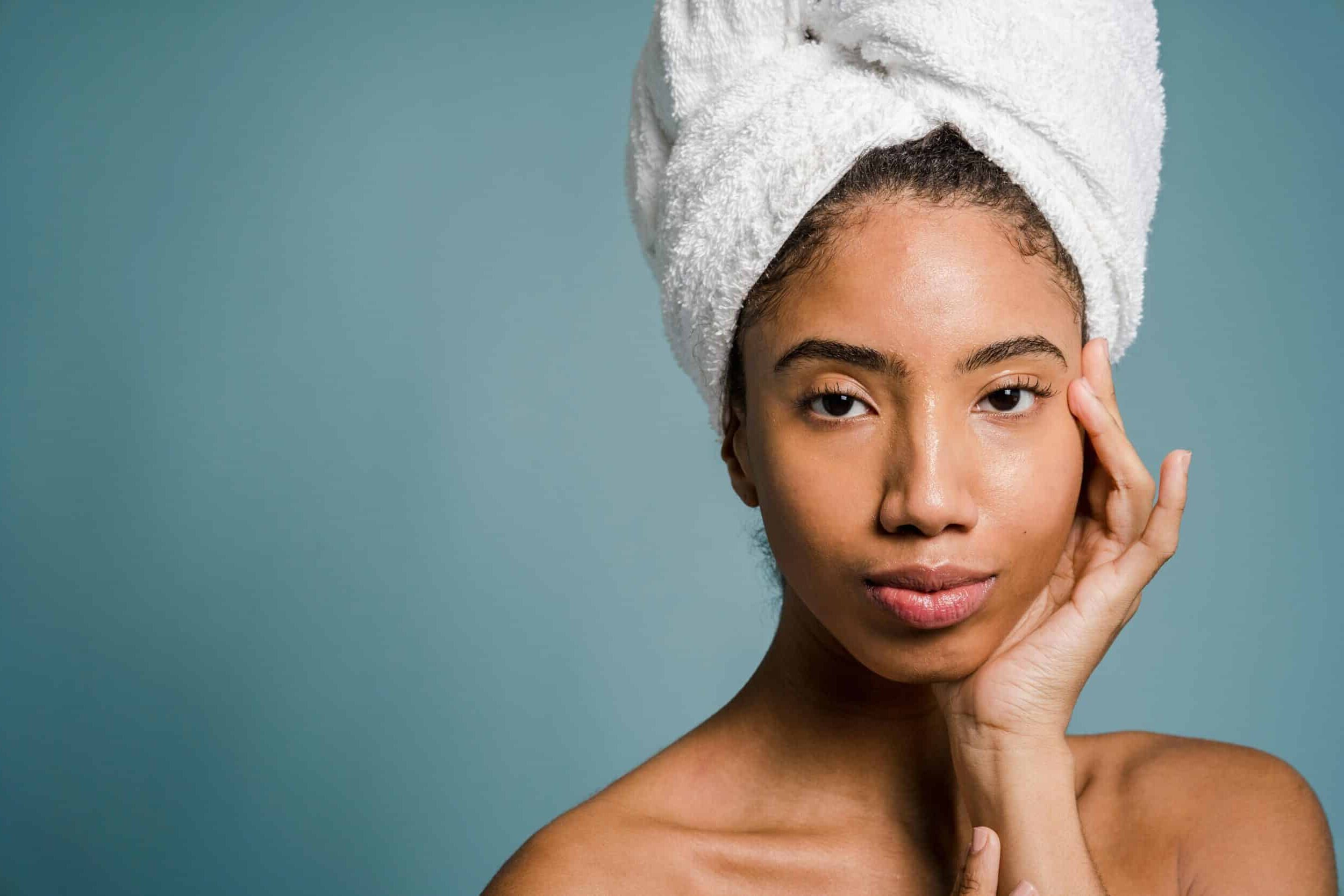 A smiling woman with a towel wrapped around her hair touching her cheek