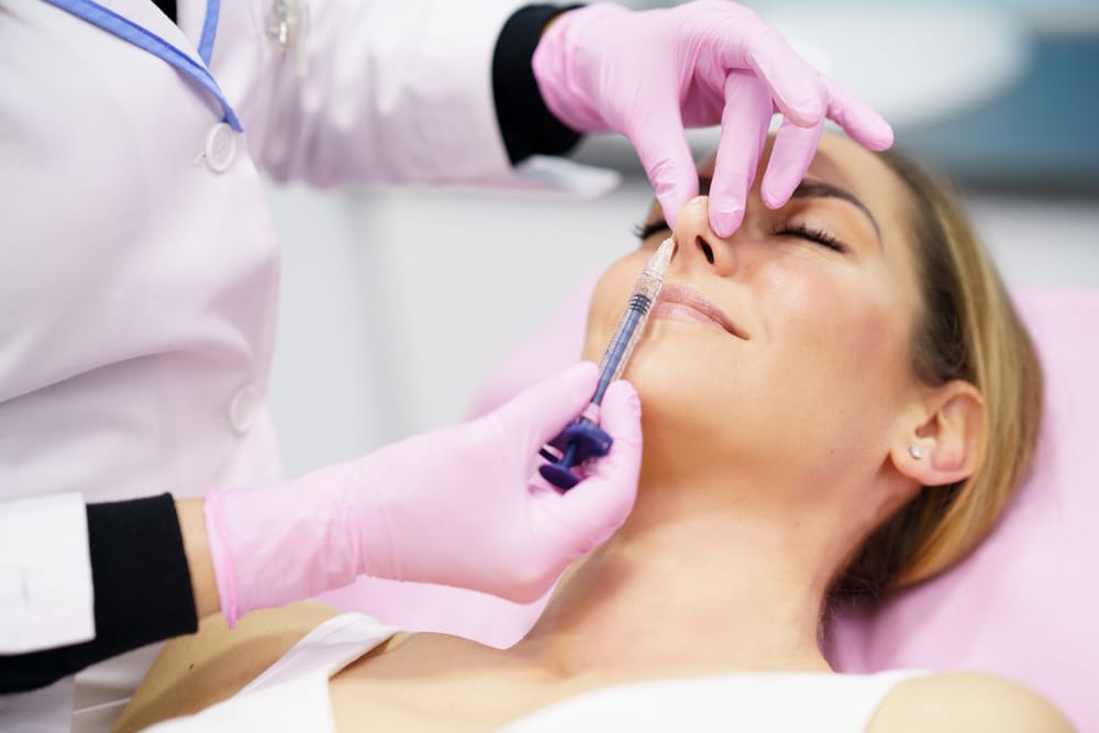 Woman smiling while receiving a liquid rhinoplasty to lift the tip of her nose.