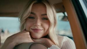 A smiling blonde model rests her chin on her hands in a car