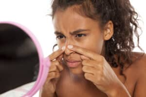 Woman touching pimple on nose while looking in mirror
