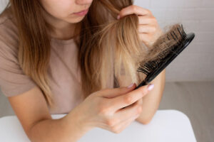 Woman examining strands of hair collected in a brush after noticing increased shedding.