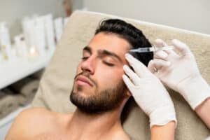 Man receiving a cosmetic injectable treatment near the temple in a clinical setting.